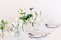 an ethereal minimalist wedding tablescape with all-neutral everything and some white blooms and greenery in jars to form a centerpiece