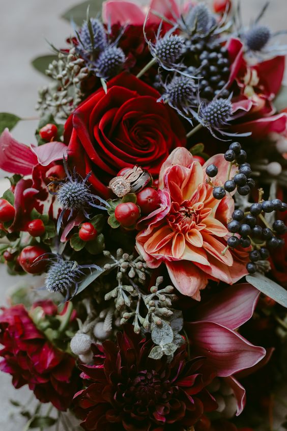 an extra bold fall wedding bouquet of deep red, fuchsia and orange blooms, berries, thistles and greenery is amazing to rock