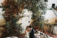 a beautiful and lush wedding arch composed of greenery and dried fall leaves is a pretty solution for a fall wedding and it will make a statement