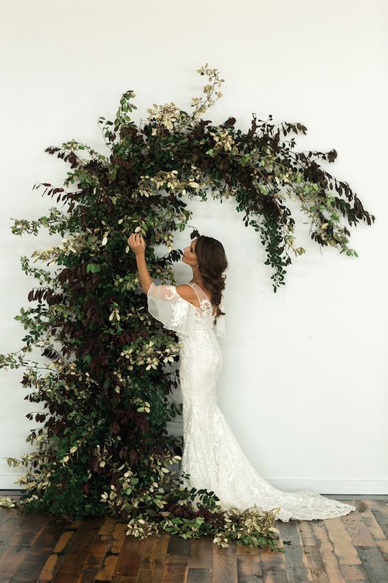 a beautiful greenery wedding altar of greenery and dark foliage with a curved top is a gorgeous idea for a fall wedding