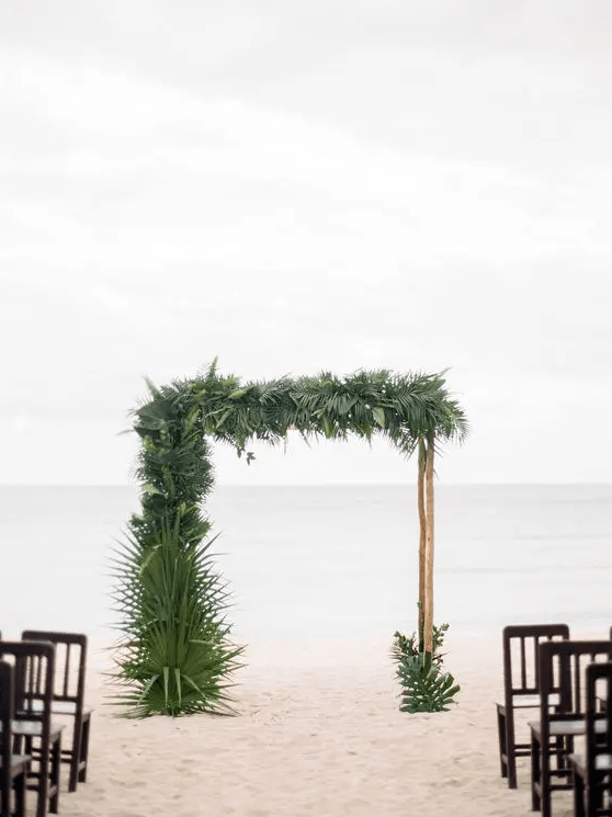 a branch wedding arch decorated with lush tropical leaves for a tropical beach wedding