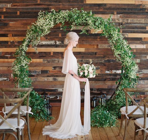 a chic lush greenery round wedding arch with white blooms and candle lanterns around is a delicate and pretty idea for your wedding