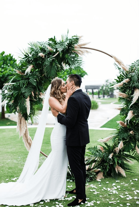 a chic tropical wedding arch covered with pampas grass and fronds is a lovely idea for a boho tropical wedding