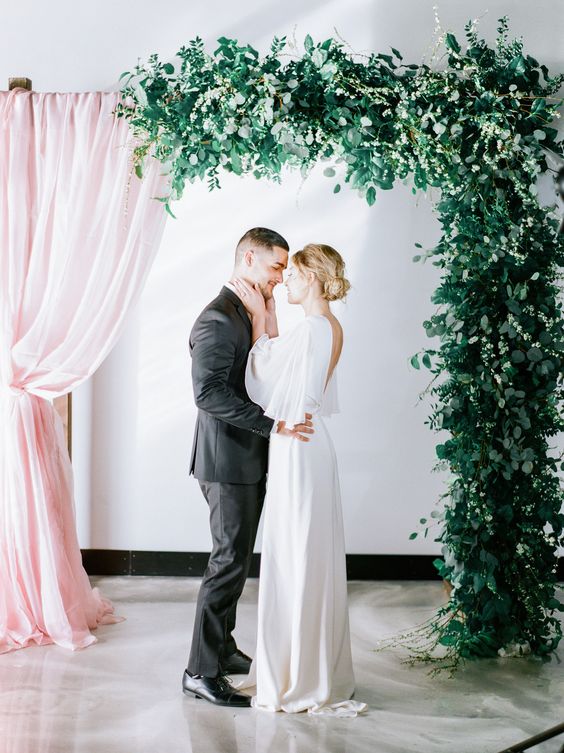 a gorgeous wedding arch with asymmetrical design   pink curtains and lush greenery is a fantastic solution for a modern wedding