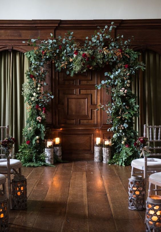 a greenery and evergreen wedding arch with some pink and burgundy blooms and stumps with candles is a chic idea for a winter wedding