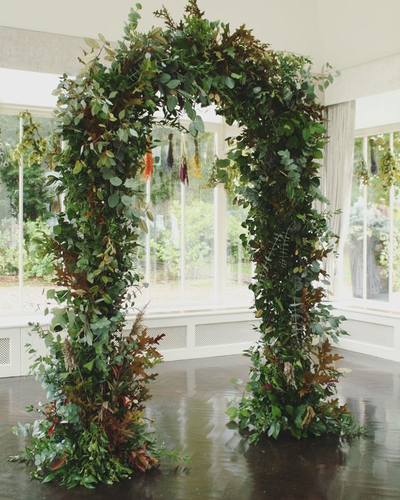a lush greenery wedding arch covered with bold fall leaves, too, is a cool idea for a modern wedding in summer or fall
