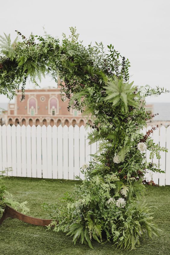 a lush round wedding arch with a lot of various greenery is a cool idea for many weddings, for indoors and outdoors