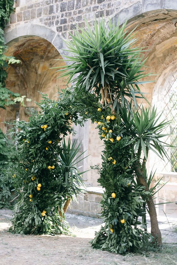 a lush tropical greenery wedding arch dotted with lemons is a cool idea for a tropical or Tuscany wedding