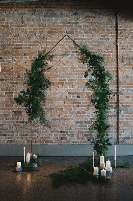 a minimalist organic wedding ceremony space with a greenery wedding arch and pillar candles on the floor