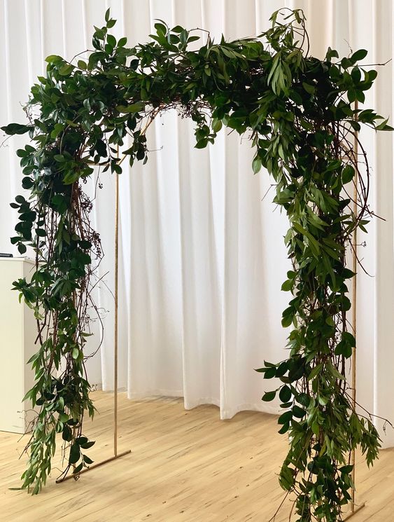 a modern wedding arch covered with greenery is a cool idea for a modern wedding, both indoors and outdoors