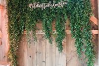 a pretty lush greenery wedding arch placed on the wall and decorated with some calligraphy is a chic idea for a rustic wedding