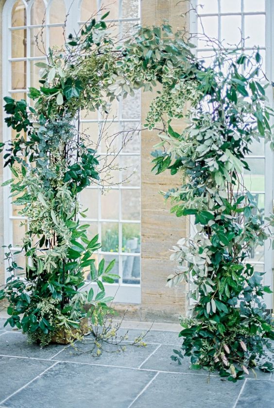 a pretty wedding arch decorated with lush and wild greenery and branches all over is a stylish idea for a nature inspired wedding