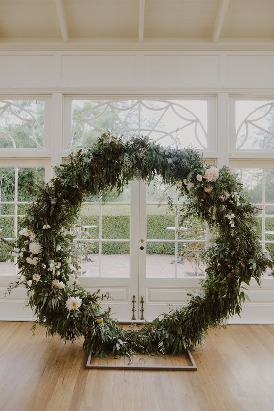 a round greenery wedding arch dotted with white blooms is a cool decoration for a summer wedding