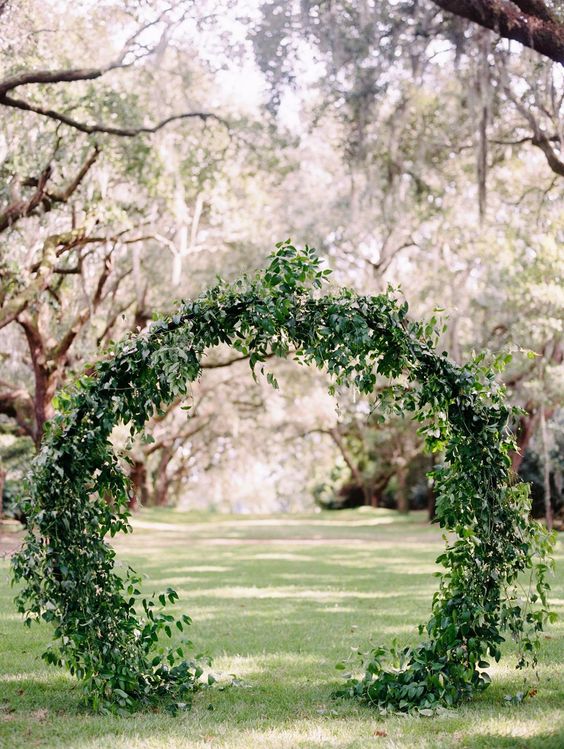 a round wedding arch fully covered with greenery and foliage is a very cool and fresh idea for your wedding