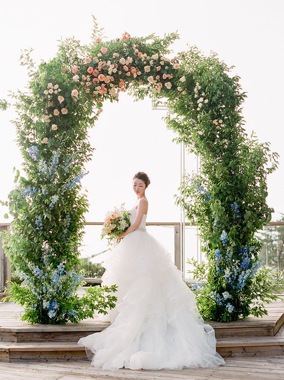 a super lush and gorgeous greenery wedding arch decorated with light blue and pink blooms is a chic and lovely idea