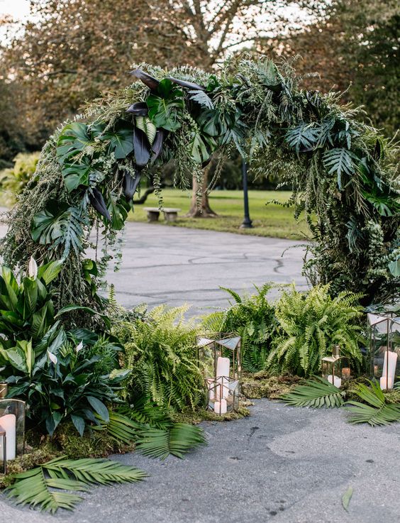 a super lush and textural round wedding arch covered with greenery and leaves plus lanterns around is amazing