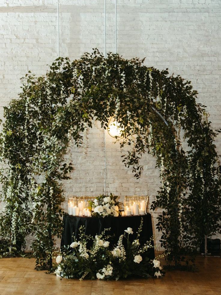 a super lush double greenery wedding arch with lights, candles and blooms is a cool idea for both indoors and outdoors