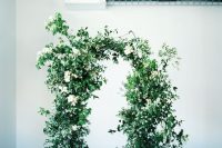 a super lush greenery wedding arch dotted with white blooms is a refined and a bit wild idea for a spring or summer wedding