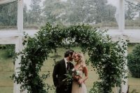 a super lush round wedding arch covered with greenery of various kinds completely looks amazing and a bit wild