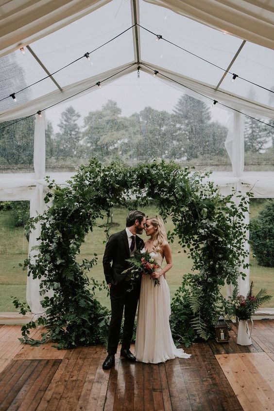 a super lush round wedding arch covered with greenery of various kinds completely looks amazing and a bit wild