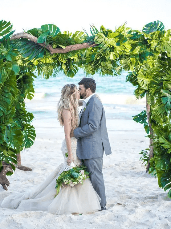 a super lush tropical wedding arch of driftwood and lush tropical leaves, with a gorgeous sea view, is a lovely idea for a tropical wedding