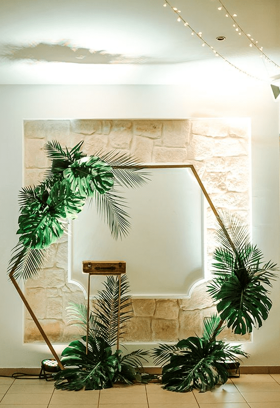 a tropical hexagon wedding arch decorated with large fronds is a pretty idea for a modern tropical wedding
