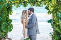 a tropical wedding arch fully covered with tropical leaves and with some branches is a great idea for a tropical beach wedding