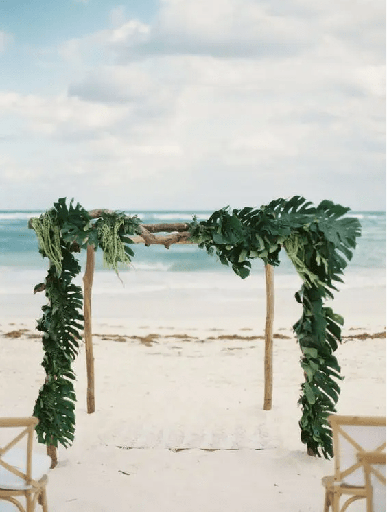 a wooden wedding arch covered fully with palm leaves for tropical beach wedding