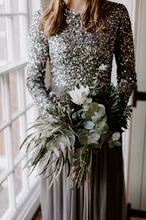 a modern glam winter bridal look with a sequin bodice and a grey layered skirt plus a textural greenery wedding bouquet