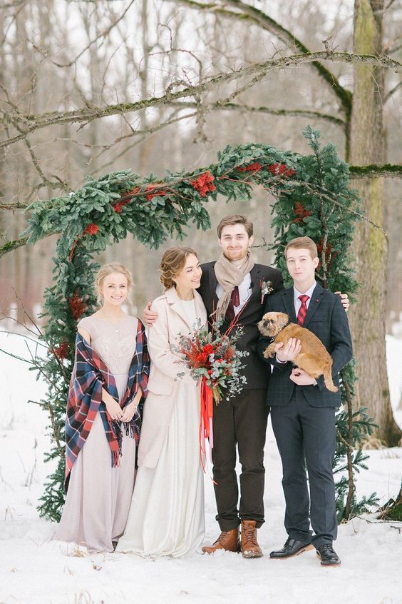 a gorgeous asymmetrical Christmas wedding arch of usual and red spray painted evergreens is a fantastic idea for a snowy holiday wedding
