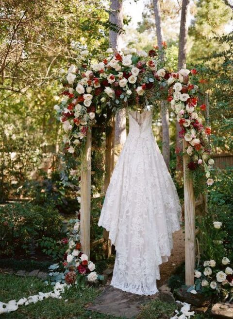 a dreamy and bold Christmas wedding arch with lush white, burgundy roses and greenery is a luxurious idea