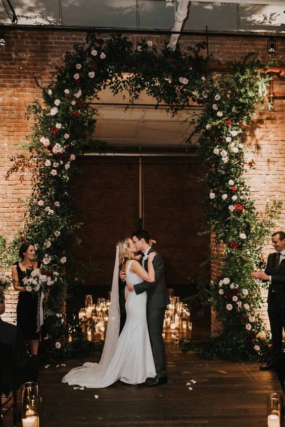 a jaw-dropping Christmas wedding arch covering the doorway, with los of greenery, blush and red blooms and floating candles is amazing