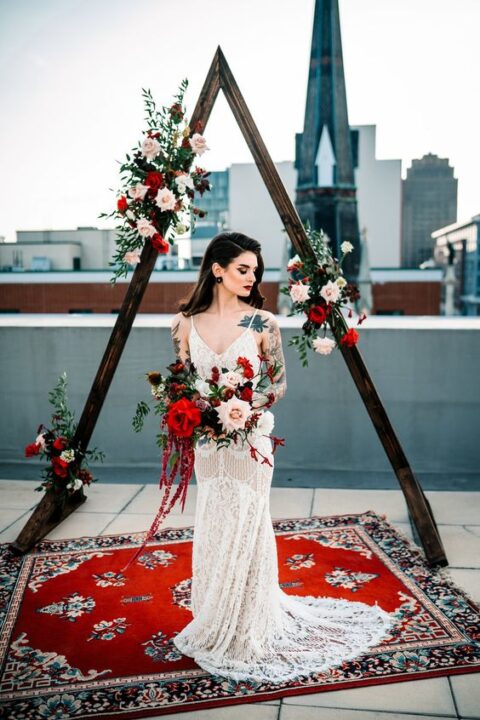 a bold Christmas wedding arch of stained wood, blush and red roses and greenery plus a bold boho rug is a stylish idea