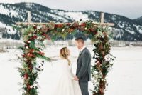 09 a beautiful Christmas wedding arch with greenery, red and burgundy blooms and dried flowers is a lovely idea for a holiday wedding