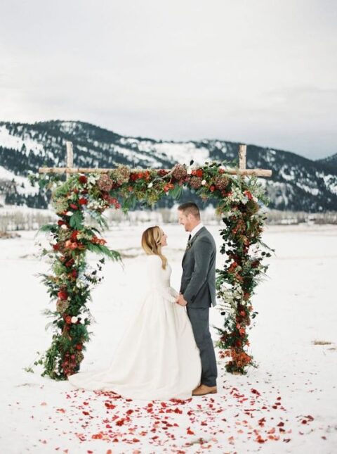 a beautiful Christmas wedding arch with greenery, red and burgundy blooms and dried flowers is a lovely idea for a holiday wedding