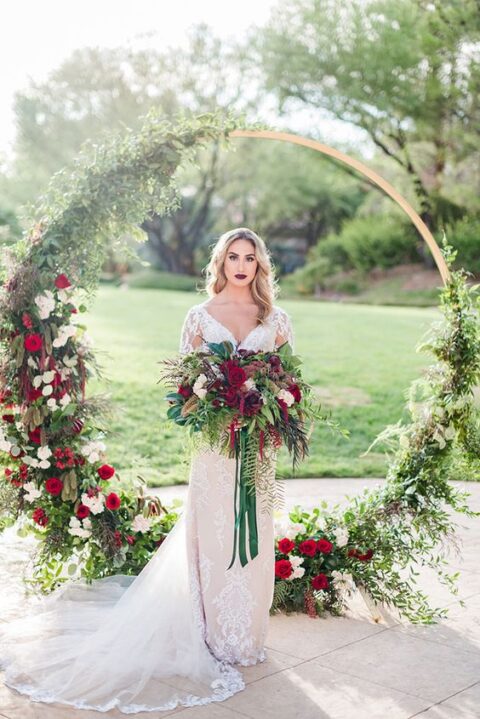 a stylish round wedding arch decorated with greenery, white and deep red blooms is an elegant idea for a Christmas wedding