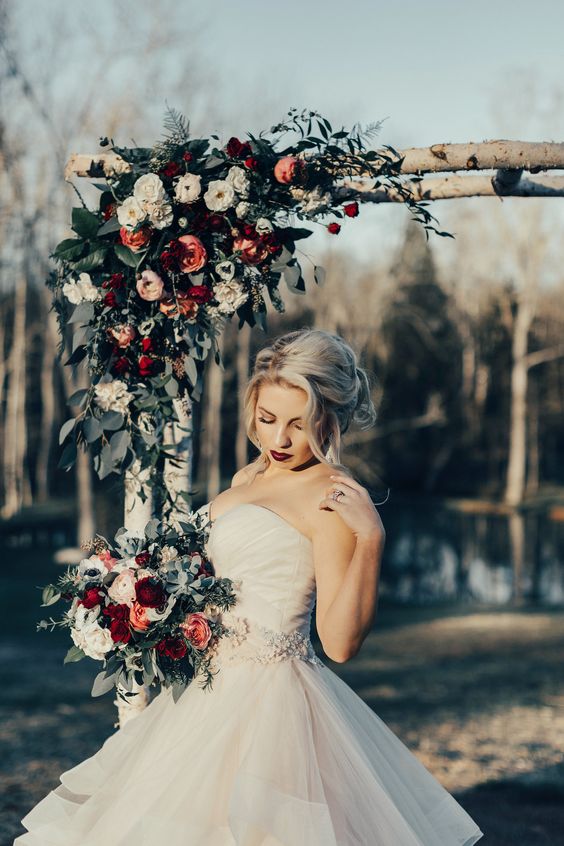 a rustic Christmas wedding arch decorated with greenery, white, blush and burgundy blooms and berries is a lovely idea for winter
