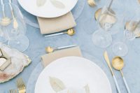 15 a beautiful winter wedding tablescape with a blue tablecloth, clear chargers and white porcelain, gold candleholders and cutlery and tan napkins