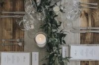 18 a chic winter wedding tablescape with a grey table runner and linens, candles, a greenery runner and elegant cutlery