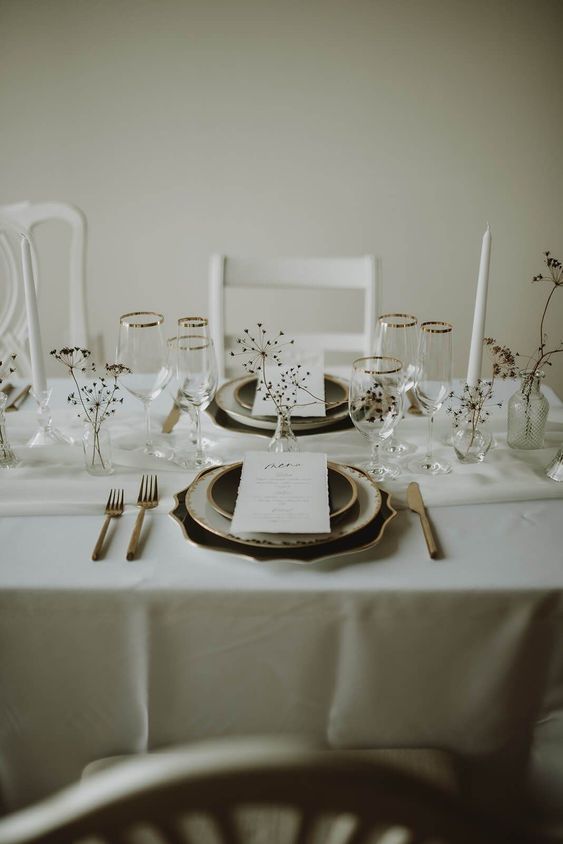 a dreamy and airy modern winter wedding tablescape with neutral linens, dried branches and blooms, black and white plates and dark cutlery