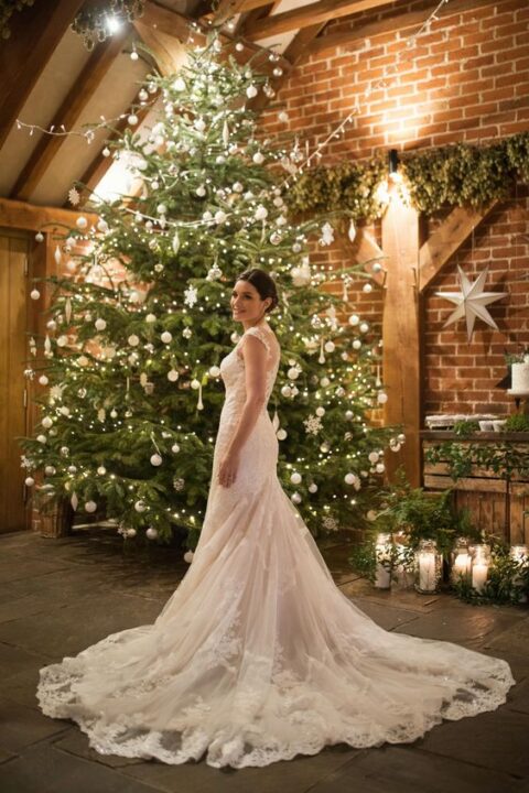a Christmas tree decorated with white ornaments and lights is a gorgeous wedding backdrop for a Christmas wedding