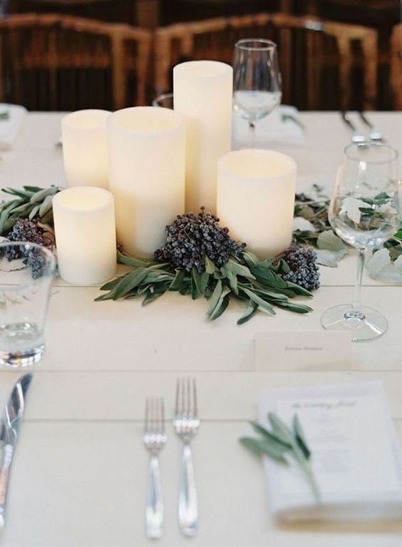 a modern winter wedding centerpiece of pillar candles, greenery and privet berries is a stylish and chic idea