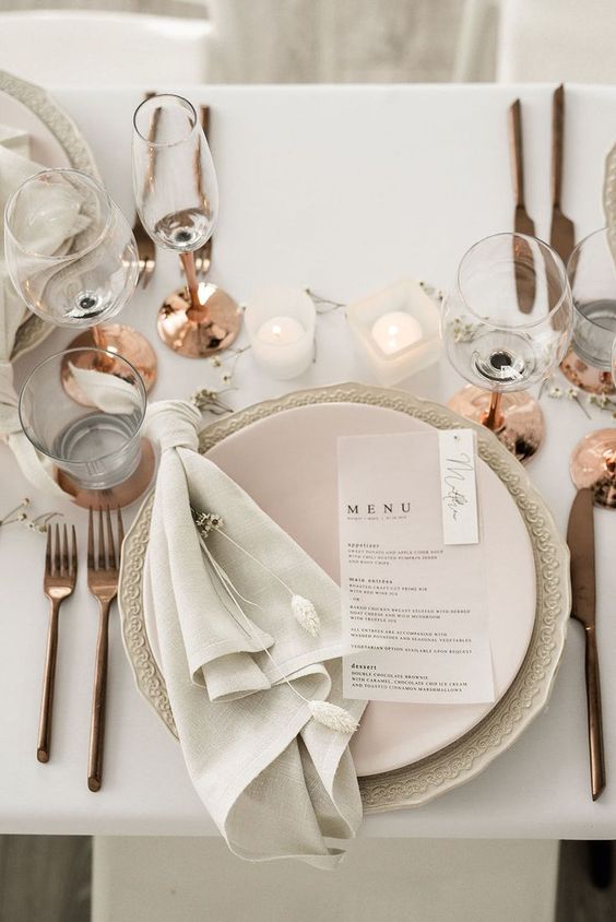 a pretty neutral winter wedding tablescape with a patterned charger, a blush plate, copper touches and candles on the table
