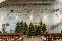 26 a pretty Christmas wedding ceremony space with a row of Christmas trees with lights as a backdrop and simple white chairs for a rustic wedding