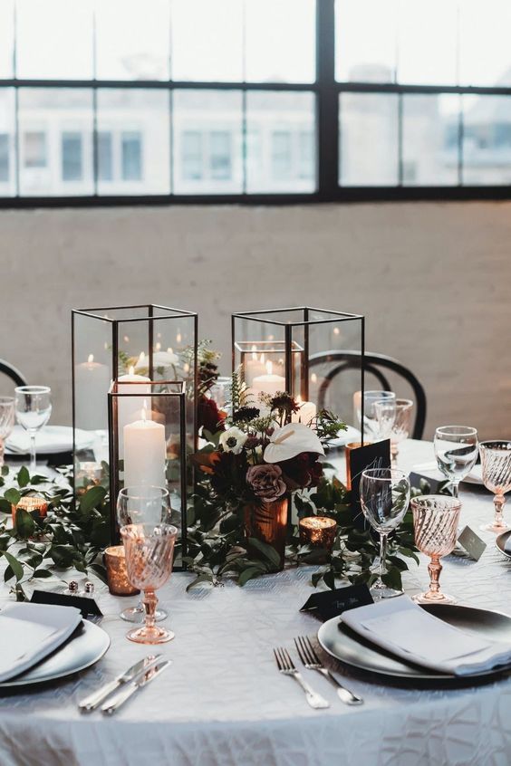a refined winter wedding tablescape with white and dusty blooms, candles in candle lanterns, colored glasses and greenery