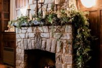 28 a stone fireplace decorated with super lush greenery and candles on tall stands is a lovely Christmas wedding backdrop idea
