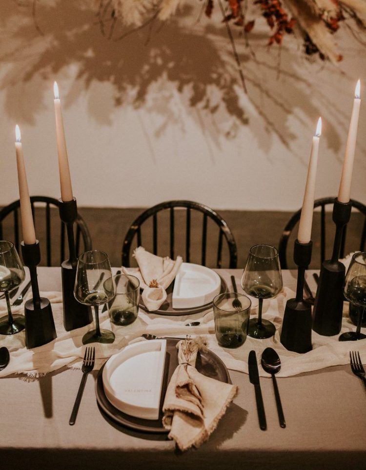 a stylish modern winter wedding tablescape with black candleholders and cutlery, grey glasses, grey and white plates and cool textural linens