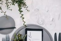 29 a stylish modern winter wedding tablescape with greenery, candles, matte grey plates, a black napkin and greenery