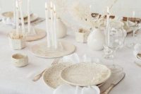 30 an airy white winter wedding tablescape with speckled plates, tall and thin white candles, dried branches with leaves and neutral linens