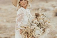 a beautiful boho bridal look with a boho lace wedding dress and a capelet, a neutral hat and a dried flower wedding bouquet for a desert wedding